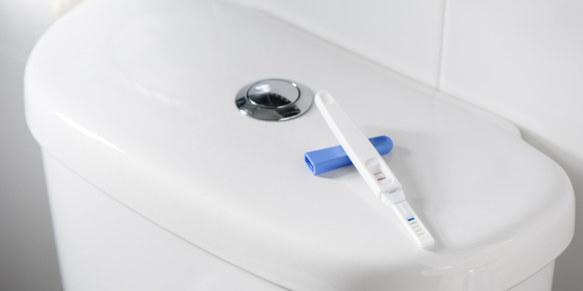 A positive pregnancy test sitting on the back of a toilet.